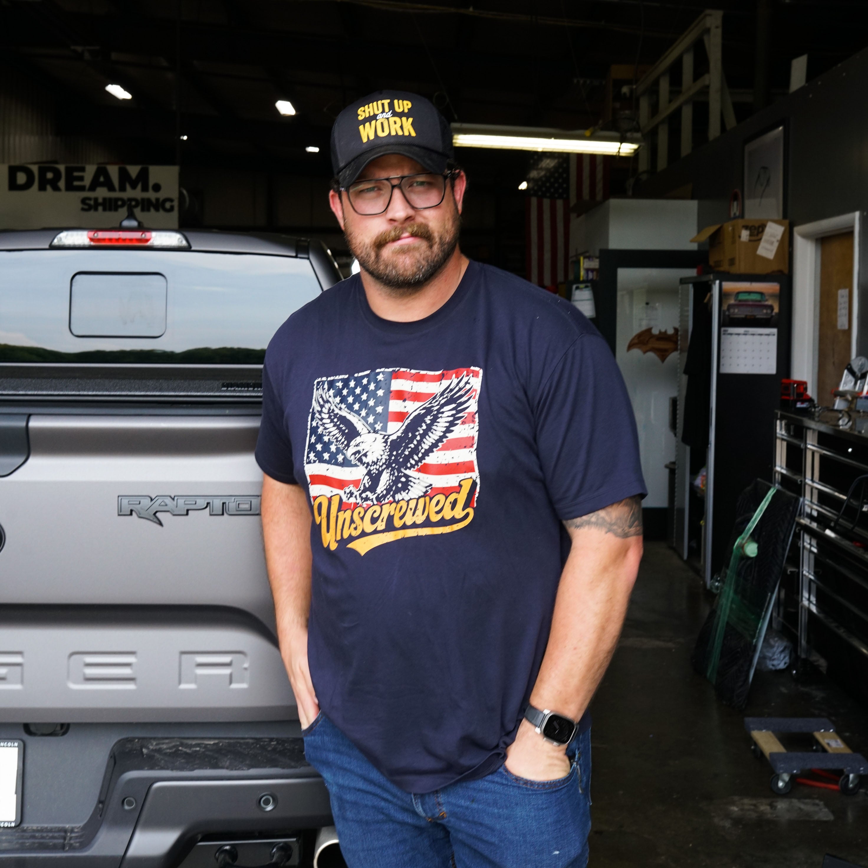 A man wearing a navy blue graphic t-shirt that says Unscrewed.