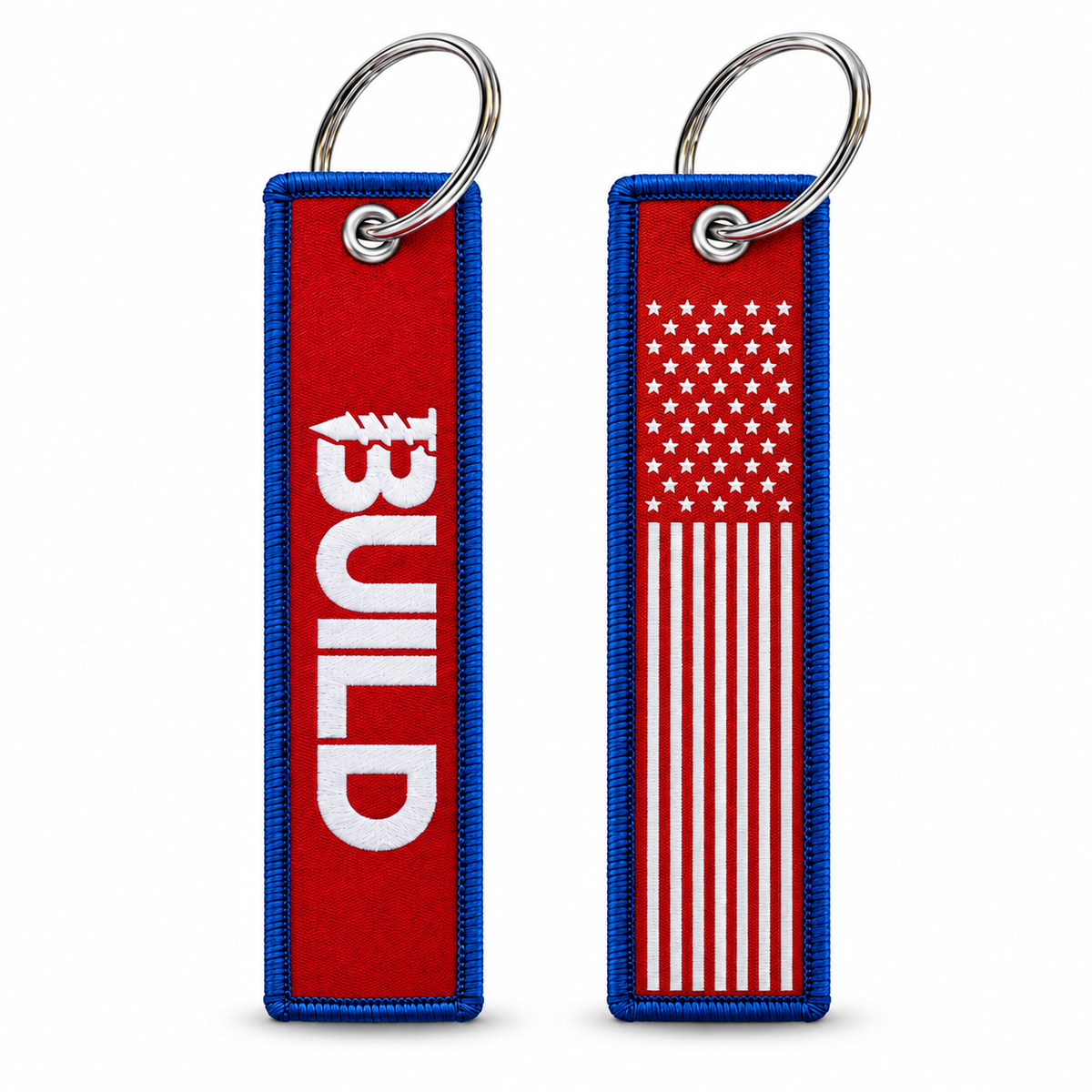 Two rectangular embroidered key tags on a white background, each with a silver metal key ring. The left tag has a red center with blue stitched edges and large white vertical text reading BUILD.