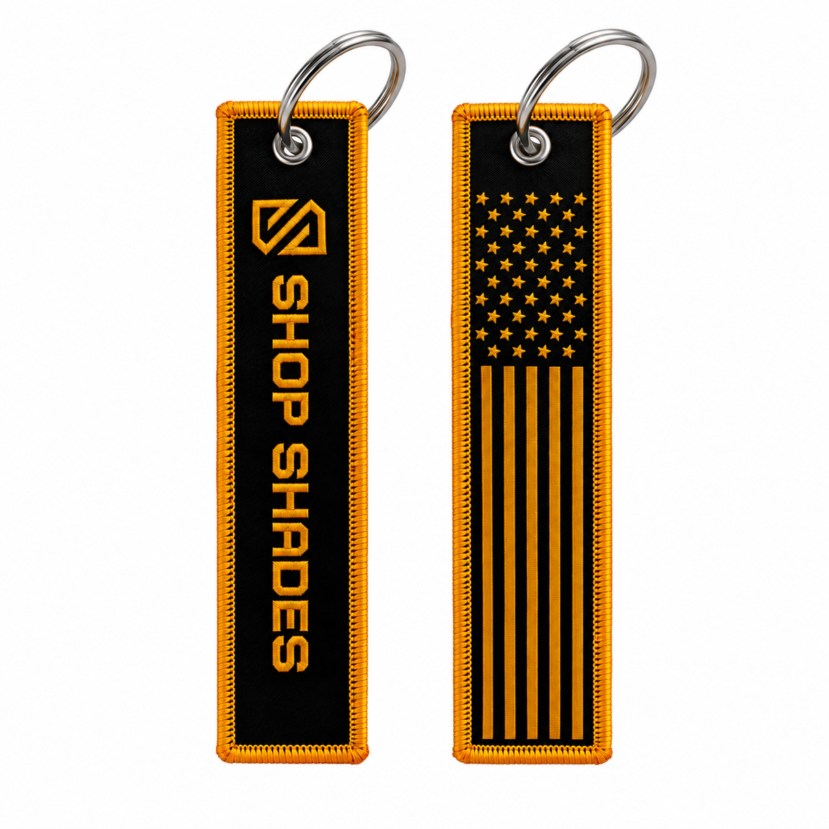Two black rectangular embroidered keychain tags with orange-yellow borders and silver metal key rings, shown side by side on a white background. One tag features the text 'SHOP SHADES' with a stylized logo, and the other features a vertical American flag design.