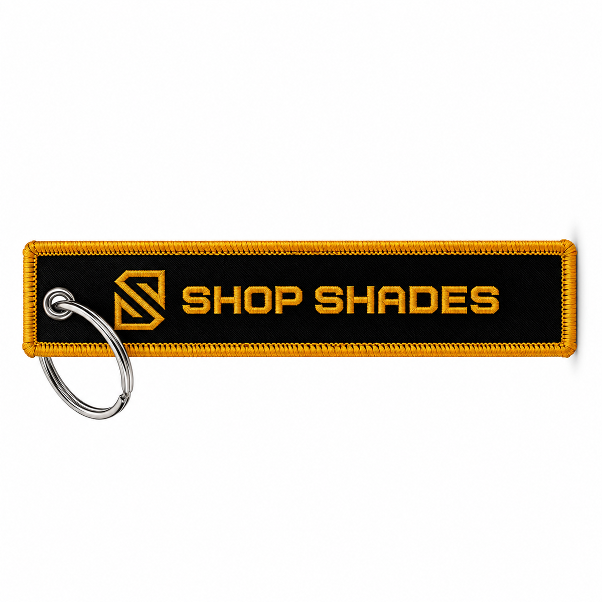 A rectangular embroidered keychain patch with a black center, yellow border, and yellow 'SHOP SHADES' text and logo, attached to a silver metal split ring on a white background.