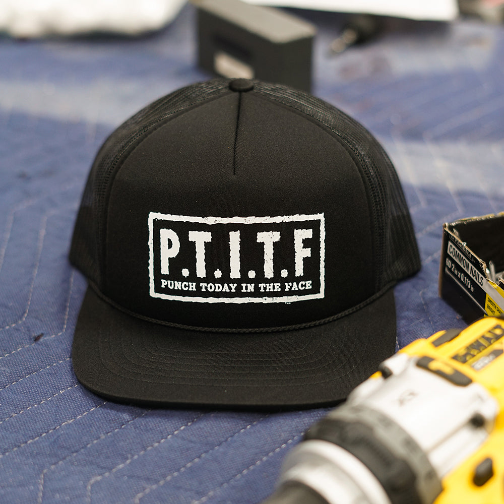 Black flat bill trucker hat with mesh back panels and "P.T.I.T.F" in a white stencil box on the front, with "Punch Today In The Face" spelled out beneath it.