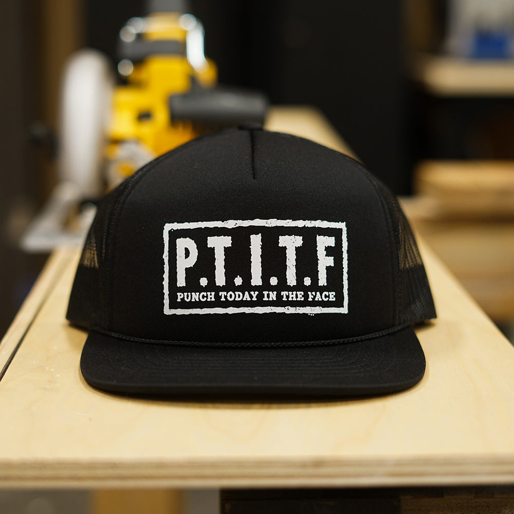 Black flat bill trucker hat with mesh back panels and "P.T.I.T.F" in a white stencil box on the front, with "Punch Today In The Face" spelled out beneath it.